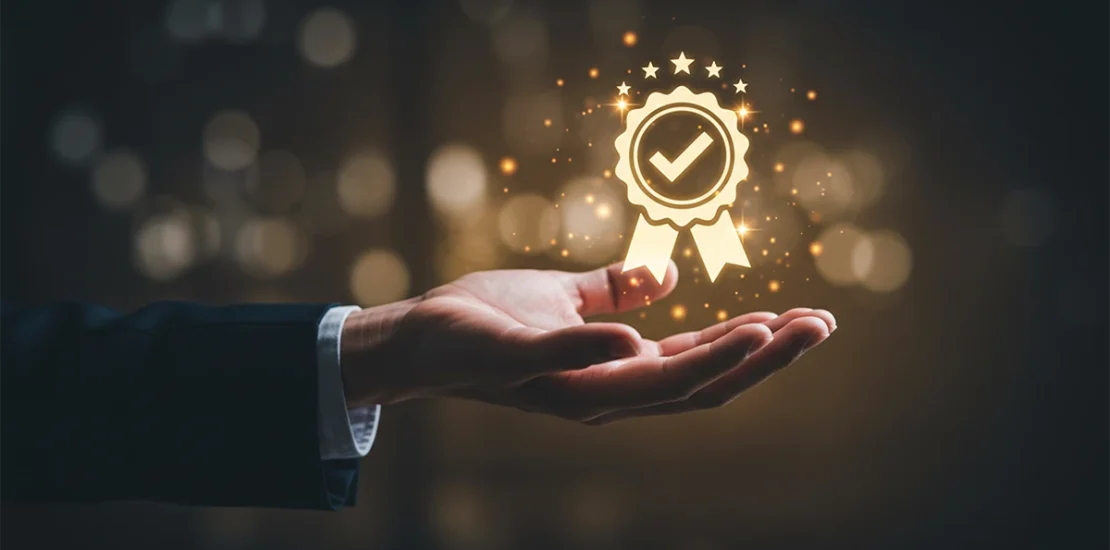 A professional's hand held out toward a glowing golden seal icon with a checkmark and stars, symbolizing the prestige of the Business Excellence Awards in UAE and a commitment to high corporate standards.
